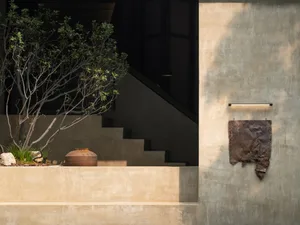 A modern staircase leads to a doorway in front of a concrete wall, flanked by two potted plants