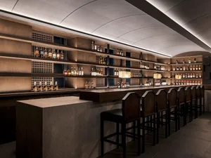 Elegant bar lounge with a long wooden counter, stools, and displayed bottles, creating a sophisticated and inviting atmosphere