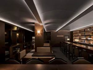 Cozy bar area with a long wooden counter, multiple stools, and dining tables, set in a warm and inviting atmosphere