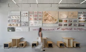 Interior design showroom with architectural drawings on walls, tables, and a woman walking through the space