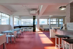 Empty restaurant interior with a red floor, white walls, and dining tables with chairs and potted plants