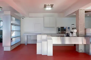 Industrial kitchen with white walls, red floors, and modern appliances, including a refrigerator, microwave, and sink
