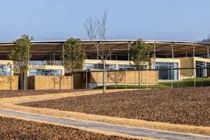 一座木造建築前方有寬敞開放空間，周圍環繞樹木與草地，傳達寧靜與大自然的連結感