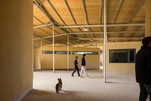 Two men walking in a calm and peaceful indoor space with a dog, surrounded by wooden floors and a serene atmosphere