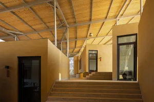 A two-story house with a yellow exterior wall, featuring windows on both levels and a wooden staircase with a railing, conveying a comfortable and welcoming living environment