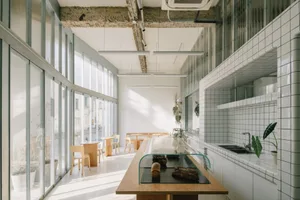 Bright and inviting open kitchen with wooden floors, white walls, a dining table, chairs, and potted plants, with natural light streaming in through the windows