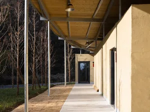 A modern hallway with a wooden floor and concrete walls, adorned with wood panels, leading to a door with two doors visible, one near the center and another towards the right side