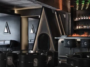Modern bar area with a black leather lounge chair, dining table, and countertop with a sink, surrounded by bottles and featuring a stylish and comfortable atmosphere