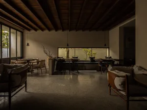 Open dining space with stone flooring, multiple tables, chairs, and potted plants, creating a modern and sophisticated atmosphere