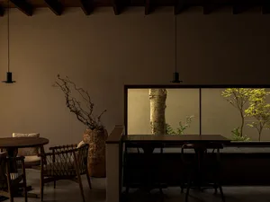 Cozy living space with a dining table, chairs, a couch, and a potted plant, set against a modern background with a wooden floor