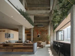 A well-lit open living space with a dining table, kitchen area, and bar counter, surrounded by artwork and multiple potted plants