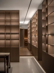 A calm and organized hallway with wooden walls and floors, lined with bookshelves and a chair, showcasing a collection of books