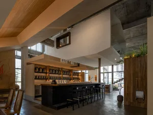 A modern restaurant kitchen with a wooden bar counter, dining table, and stools, featuring various decorative items and a warm atmosphere