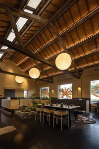 A modern restaurant dining area with tables, chairs, potted plants, hanging lights, and artwork on the walls