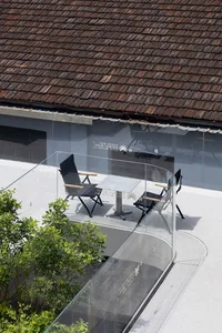 A glass table in a metal frame is surrounded by chairs in an outdoor patio setting with trees in the background