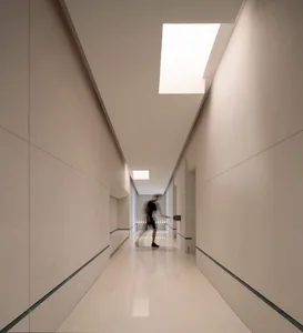 A calm and quiet hallway with a white tile floor and overhead lighting, two people walking in the distance