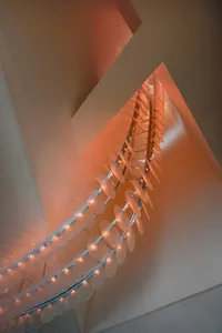 A modern stairwell with a glass chain link fence, illuminated by lights, creating a striking contrast between transparent and opaque elements