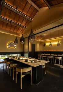 A warm and inviting Asian restaurant interior with a long dining table, chairs, and wooden elements, set for a meal with bowls and cups