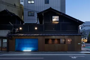 A traditional Asian-style house with a wooden exterior, featuring large and small windows, two doors, and a black roof, set in a cozy living environment