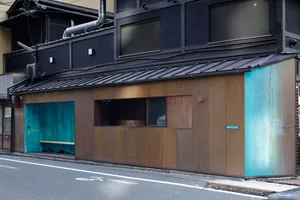 A traditional building with a brown wooden facade, blue door, and two windows, set against a bright daytime atmosphere