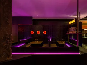 Purple-lit bathroom with a black marble countertop, three sinks, and orange circles above each sink