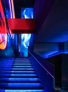 A futuristic and minimalist metal staircase leads downward into a darker area, creating a sense of depth and intrigue