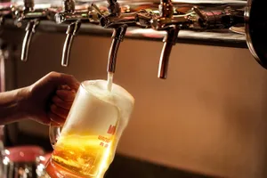 A person stands near a bar with several taps, enjoying a glass of beer