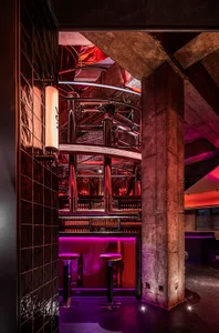 Industrial-style bar area with purple ambiance, red brick walls, and a metal wine cellar, well-lit for a warm atmosphere
