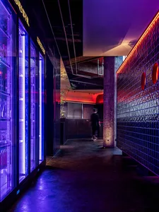 A lively restaurant and bar space with exposed brick walls, refrigerators, and a well-stocked bar with scattered bottles, set in a social atmosphere