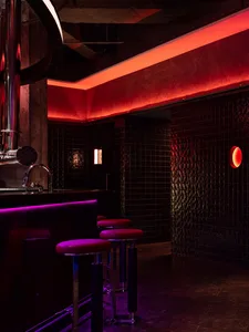 A modern bar area with a counter, stools, and sink, featuring black tile walls and inviting seating for patrons