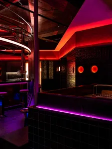 A lively bar with a purple neon glow, circular decorations, a counter with stools, and a sink, creating a welcoming atmosphere