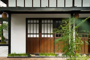 A simple Asian-style house with wooden doors and windows, surrounded by greenery and a clean white exterior