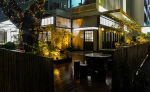 A modern Asian restaurant with a wooden deck, black table, and potted plants, set in a well-lit atmosphere