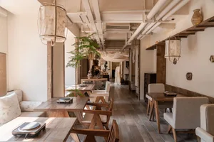 Modern restaurant interior with wooden floors and walls, featuring dining tables and chairs in a warm and inviting atmosphere