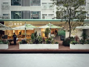 An outdoor cafe with umbrellas, potted plants, chairs, and dining tables, set against a background of refrigerators and a pleasant atmosphere