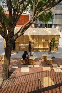 A casual outdoor seating area with a wooden bench and tables, surrounded by people socializing and enjoying the outdoors