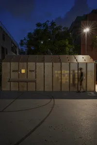 A wooden cabin with a bench outside the entrance, featuring two people standing near the building, conveying a sense of warmth and invitation