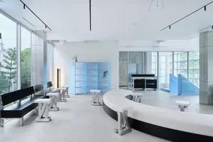 A well-lit, open room with a circular table and chairs, surrounded by natural light from windows