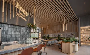 Modern restaurant interior with wooden beams, chairs, potted plants, and a lively atmosphere