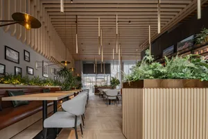 Cozy restaurant interior with wooden floors and walls, dining tables, chairs, and potted plants, lit by hanging lights