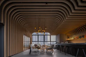 Modern living space with wooden floors and ceiling beams, surrounded by a dining table, chairs, a couch, and a bar, with multiple potted plants adding to its cozy ambiance