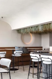 A restaurant interior with wooden tables and chairs, a grass ceiling, and multiple tables and chairs arranged throughout the room