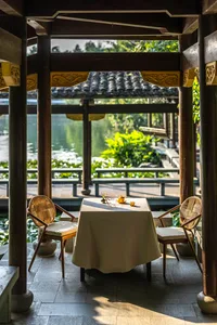 An Asian-style patio area with a dining table and chairs under a wooden pavilion, surrounded by a relaxed and inviting atmosphere