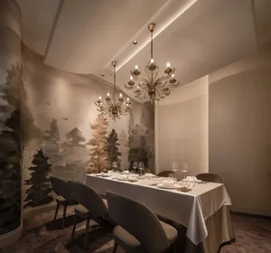 A dining area with a wooden table and chairs, set with wine glasses, cups, bowls, utensils, and bottles, creating a sophisticated and inviting atmosphere