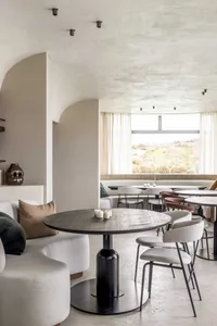 Cozy dining area with tables, chairs, couches, potted plants, and a mix of wood and metal materials in a modern and stylish setting