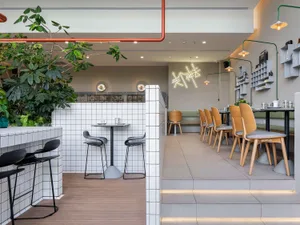 Modern restaurant interior with a dining area featuring tables, chairs, and potted plants, creating a welcoming atmosphere