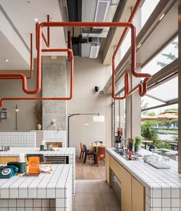 A modern kitchen with red pipes, wooden floors, and white walls, featuring a dining table and various decorative items