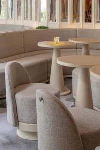 Cozy living area with three grey couches, two dining tables, and a potted plant, set against a neutral background