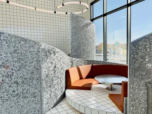 A modern restaurant with a circular dining area, stone-textured walls, and two seating areas, creating an inviting atmosphere for socializing and dining