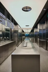 Industrial kitchen with stainless steel surfaces, two sinks, and various kitchenware and bottles, with a focus on functionality and efficiency